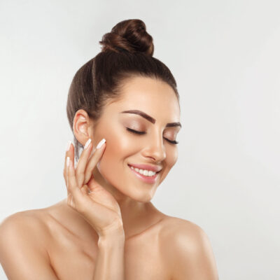 Beautiful young woman with clean perfect skin. Portrait of beauty model with natural nude make up and touching her face. Spa, skincare and wellness. Close up, copyspace.